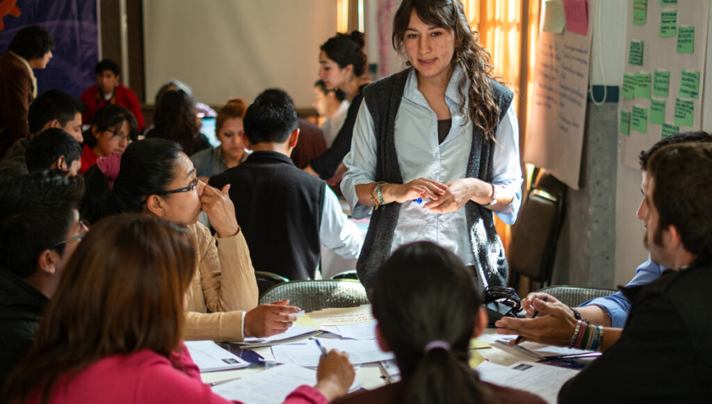 A young leader talks to a table of people at a community meeting