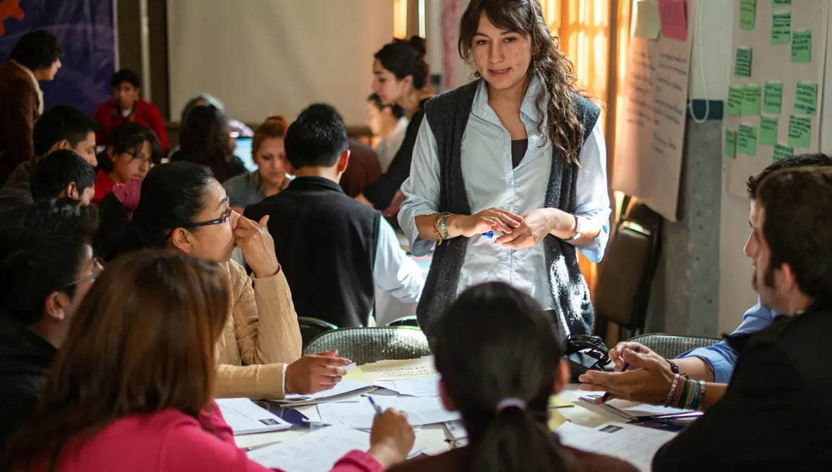 A young leader talks to a table of people at a community meeting