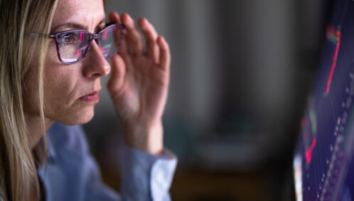 Close-up photo of a woman wearing glasses, looking with concern at a computer screen