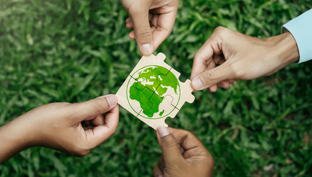 Four hands reach toward the center of the photo, each holding an interlocking puzzle piece showing a picture of the globe