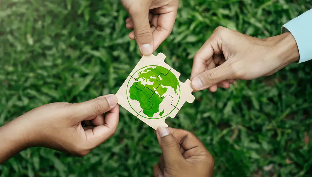 Four hands reach toward the center of the photo, each holding an interlocking puzzle piece showing a picture of the globe