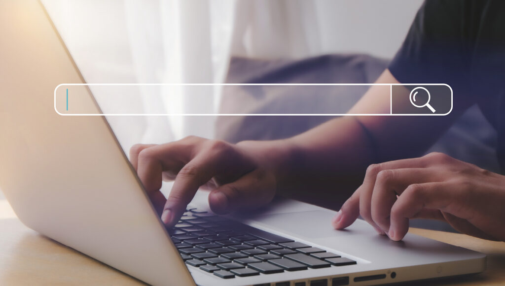 Close-up photo of hands typing on a laptop computer. Overlaid on the image is an internet search bar.