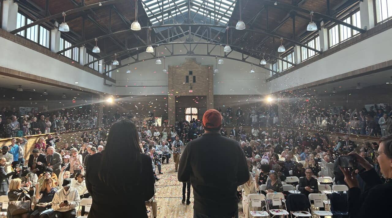 A room filled with people sitting at tables in lines, with confetti falling through the air.